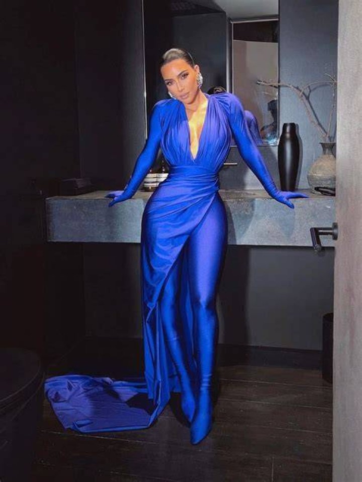 Kim leaning against a grey marble sink in a form fitting blue cat suit