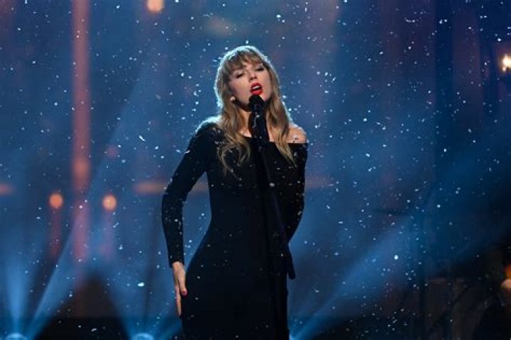Taylor Swift singing on stage with a guitar surrounded by the set of an overgrown house